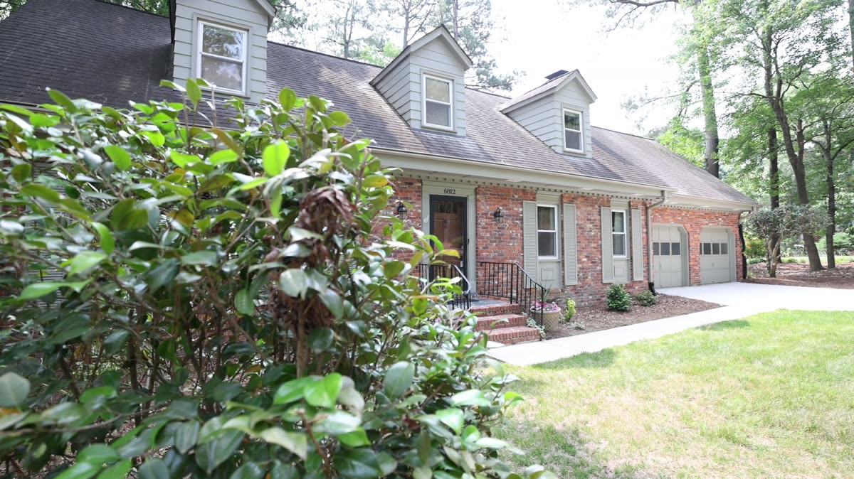 A brick single-family home with a driveway and mature trees